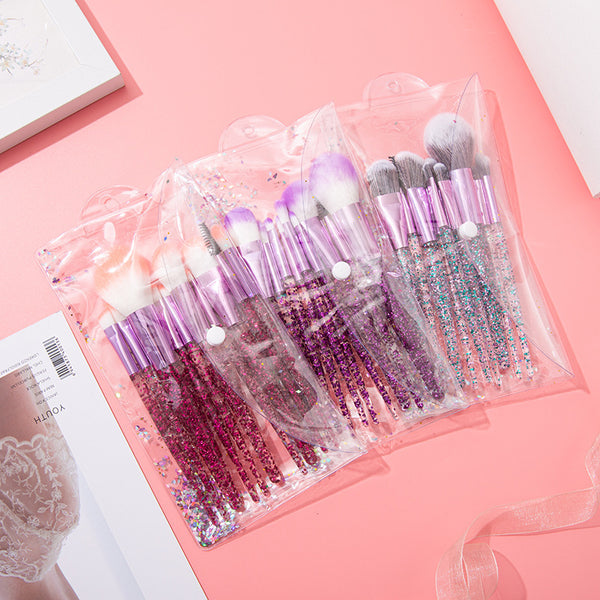 10pcs Clear Crystal Quicksand Makeup Brush Set displayed in a clear pouch with glittering handles on a pink background.