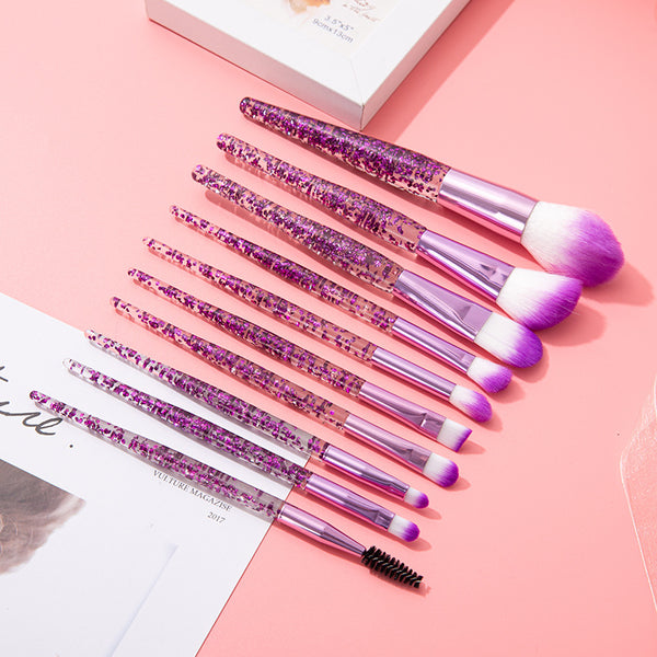 10pcs Clear Crystal Quicksand Makeup Brush Set with pink and purple glitter handles on a pink background.
