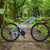 Mountain Bike with Suspension Fork & Triple Chainset on a forest trail, showcasing rugged design and performance.