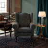 Serena Grey Fabric Wingback Chair in a stylish living room setting with a lamp and side table.