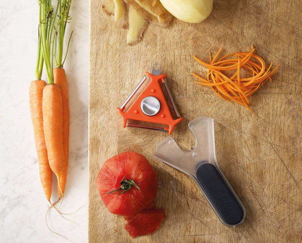 3 in 1 Peeler with Potato Eye Remover on a wooden board next to fresh carrots and tomatoes.
