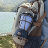 Outdoor Flicker LED Lantern attached to a backpack by a lake, providing warm ambient lighting for outdoor activities.