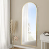 Arched Full Length Floor Mirror with Gold Frame leaning against a beige wall, reflecting natural light and creating a spacious feel.