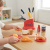 Child using the Happy Little Chef Kitchen Helper Playset for Kids with toy food and utensils on a table.