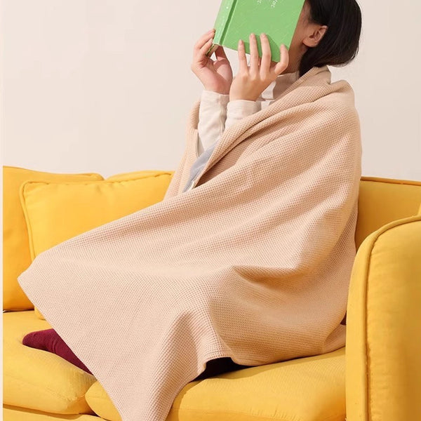 A person wearing a Portable Wearable Electric Heated Shawl Blanket while reading on a yellow couch.