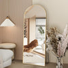 Arched Full Length Floor Mirror with Gold Frame reflecting light in a modern living room setting