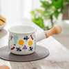 Small Enamel Milk and Butter Warming Pot with colorful fruit designs on a kitchen table.