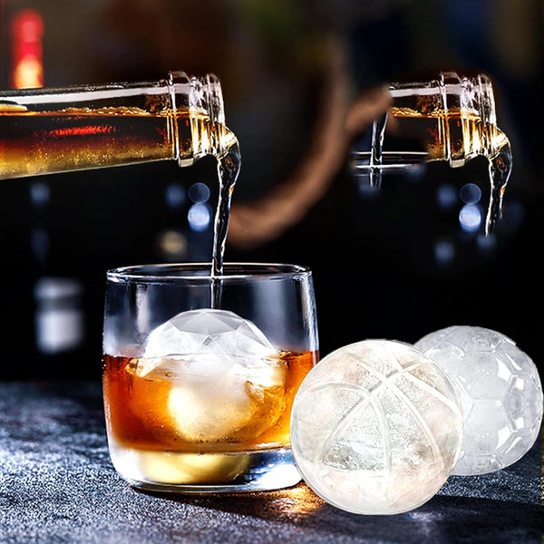 Pouring drink into a glass with Sports Ice Ball Molds in football and basketball shapes beside it.