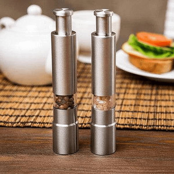 Chef Master Adjustable Salt & Pepper Grinder set on a table with a tea pot and sandwich in the background.