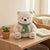23cm Plush Polar Bear sitting on a shelf with a green scarf and a small plant nearby.