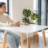 A person sitting at a Modern Nordic Dining Table, enjoying a cup of coffee in a bright, stylish interior.