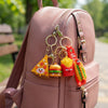 Snack Pop 3D Fast-Food Keychain collection on a pink backpack, featuring pizza, burger, fries, and hot dog.