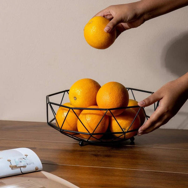 Geometric Iron Fruit Storage Basket with fresh oranges being placed inside on a wooden table.