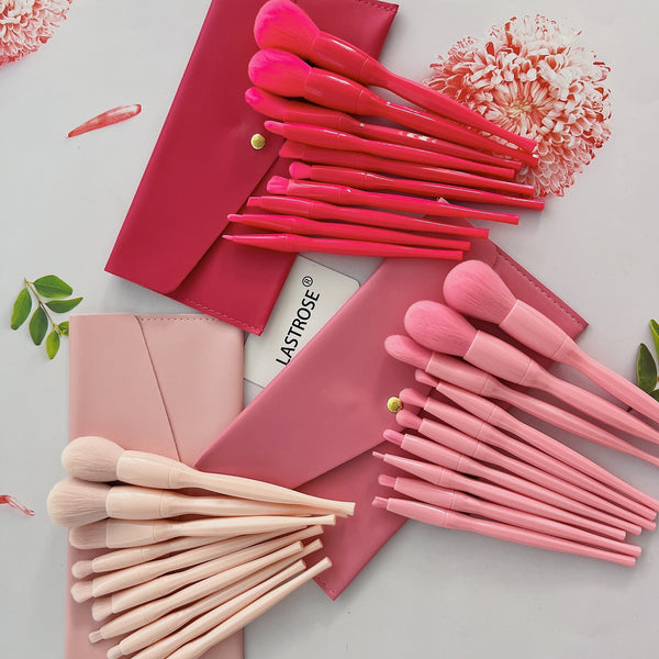 Candy colored makeup brush set displayed with pink pouches and various brushes arranged on a flat surface.