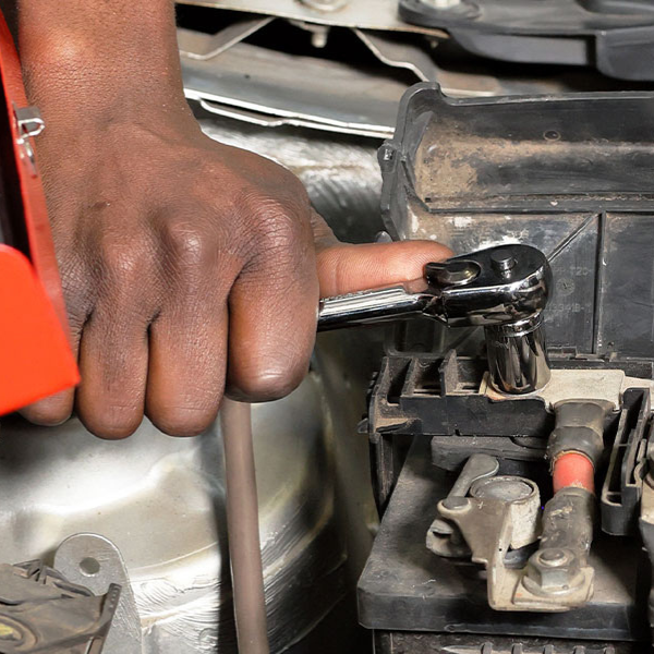 Hand using a tool from the 4-Piece Quick-Release Ratchet and Spark Plug Socket Set on a car battery.