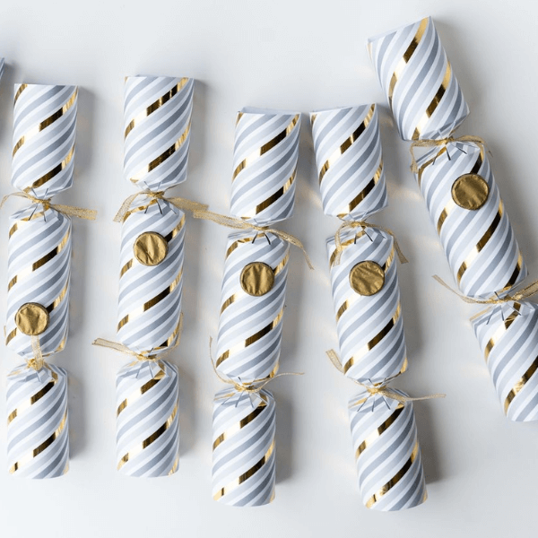 Festive Christmas Popper Crackers arranged neatly in a row, featuring elegant white and gold striped designs.