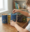 Kiddies Money Bank Tin with Coin Slot being used by a child to save coins in a colorful setting.