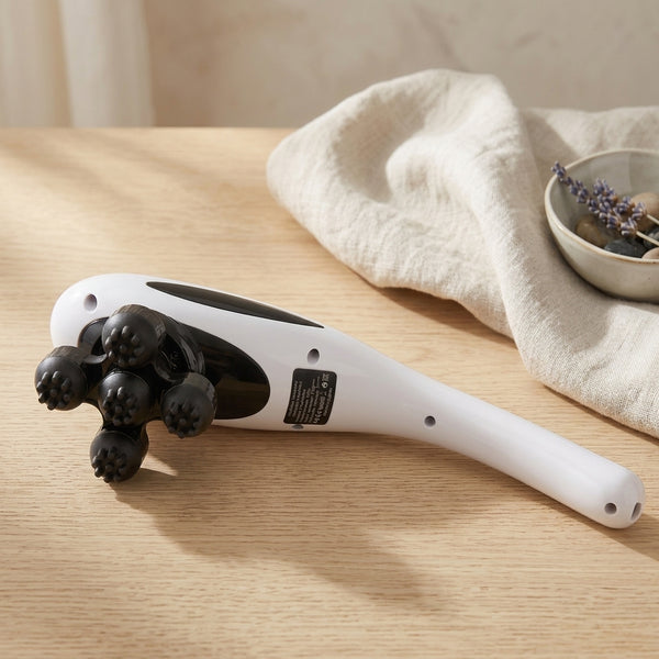 5-Head Handheld Massager resting on a tabletop with a soft fabric and decorative bowl in the background.