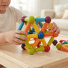 Child building with the Rainbow Magnetic Construction Sticks & Balls Set on a wooden table, creating colorful geometric shapes.