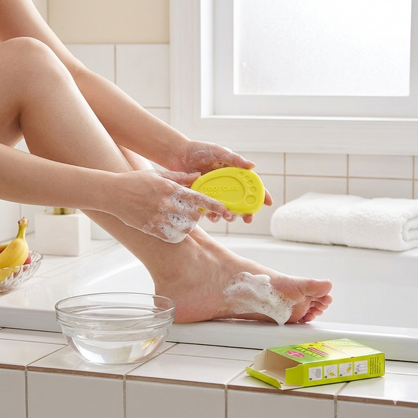 Person using Beauty Banana Milk Mini Whitening Soap for foot care in a bathroom setting.