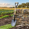 Heavy-Duty Wooden Handle Garden Shovel leaning against a stone wall in a lush garden setting.