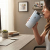 Woman sipping from a 350ml Stainless Steel Travel Mug at a desk with a computer.