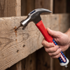 Using a Polished 16oz Claw Hammer with Shock-Reduction Grip to drive a nail into wooden planks.