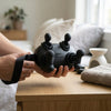 Person holding the 4-Head Handheld Body Massager on a wooden table with a cozy home setting.