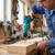 Man using a 550W High-Performance Electric Impact Drill on wood in a workshop, showing wood shavings.