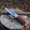 Wooden Handle Folding Tactical Pocket Knife resting on a log in a natural setting, showcasing its sleek design.