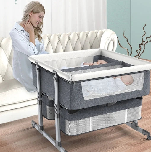 Double Crib Movable Portable Easy Fold Twins Baby Bed with two sleeping infants next to a woman on a couch.