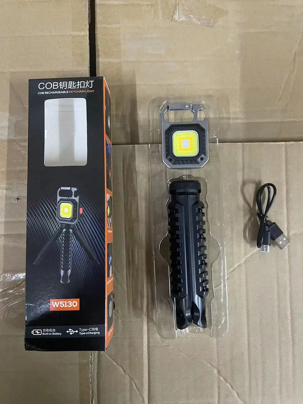 Portable COB LED Keychain Work Light with tripod and charger on cardboard background.