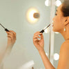 Round Portable Rechargeable Sensor Night Light illuminating a woman applying mascara in front of a mirror.