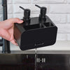 Hand holding a Waterproof Durable Portable Dispenser above a kitchen sink, showcasing its sleek black design and soap dispensing feature.