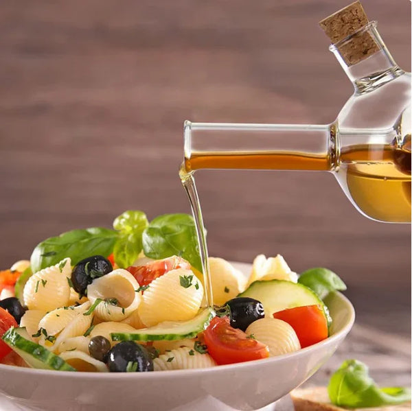 2 in 1 Olive Oil Vinegar Bottle Dispenser pouring olive oil over a fresh pasta salad garnished with vegetables.