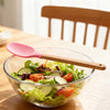 Silicone Cooking Spoon with Wooden Handle resting beside a fresh salad in a bowl on a wooden table.
