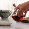 A person pouring liquid from a Dual-Core Borosilicate Glass Oil & Vinegar Dispenser into a plate.