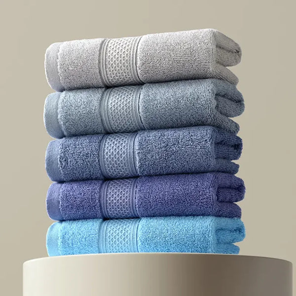 Stack of various thick cotton face and hand towels in shades of gray and blue, showcasing softness and absorbency.