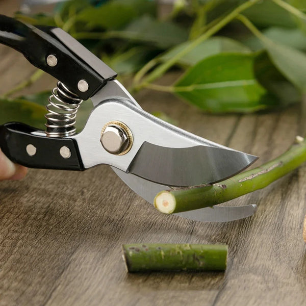 Steel Garden Bypass Pruner cutting a green branch on a wooden surface, demonstrating its heavy-duty design.