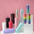Assorted Matte Black Studded Bling Cup Tumblers in various colors displayed on pedestals with a pink background.