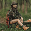 Girl sitting on a Collapsible Portable Camping Stool in a forest, wearing camouflage and enjoying the outdoors.