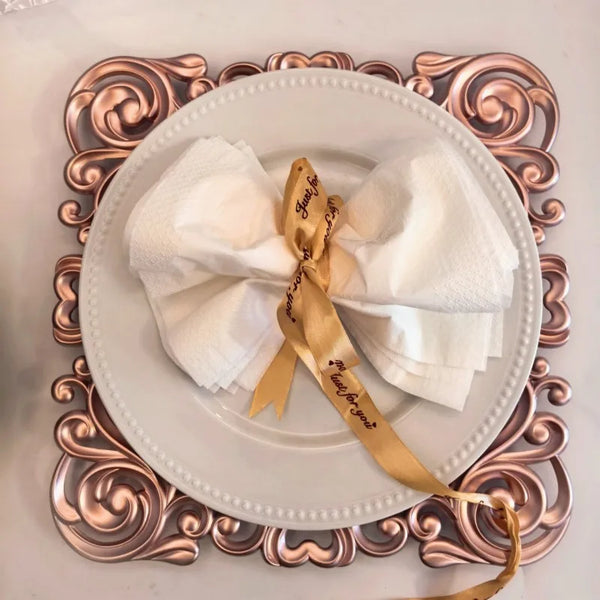 Luxury 12 Inch Eco-Friendly Disposable Round Plate with rolled napkins and ribbon on an ornate charger.