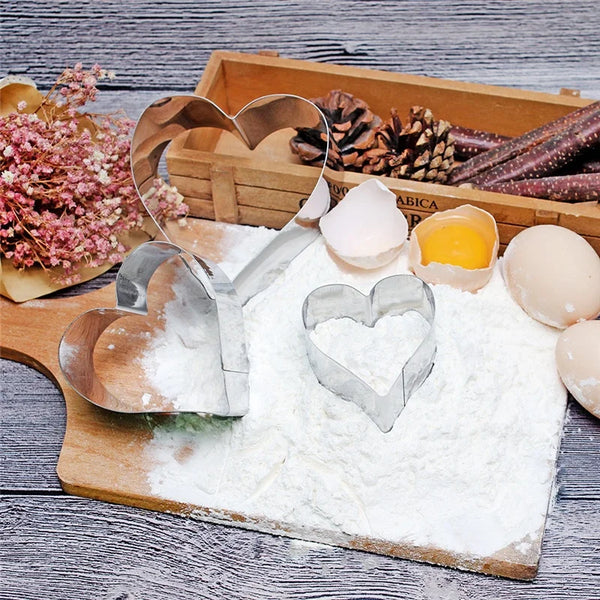 3 Piece Stainless Steel Heart Shape Cookie Cutter Set displayed on a wooden board with flour and baking ingredients.