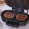 Home Mini Panini Sandwich Machine grilling two beef patties on a countertop.