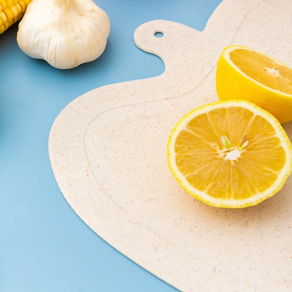 Apple Shape Plastic Cutting Board with a sliced lemon and garlic on a blue background