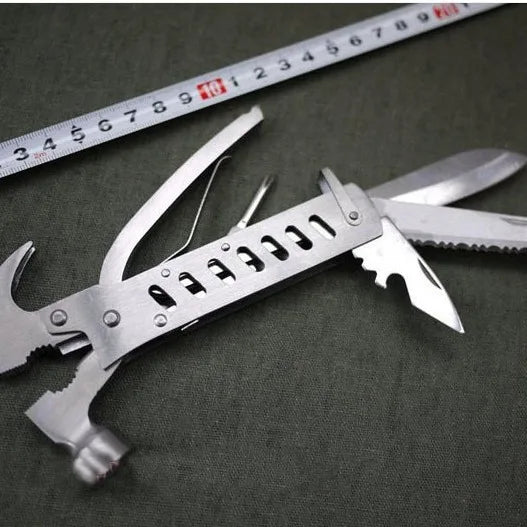 Outdoor Multi-Function Mini Claw Hammer lying on green fabric next to a measuring tape, showcasing its versatile design.