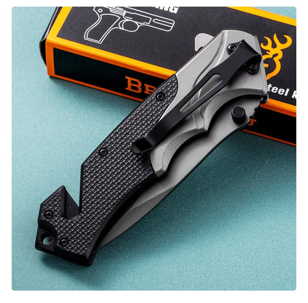 G10 Stainless Steel Folding Hunting Knife resting on a green surface next to its packaging.