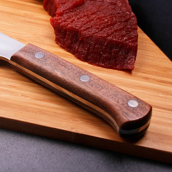 Handmade Forged Heavy Duty Cleaver with wooden handle beside a thick piece of meat on a wooden cutting board.