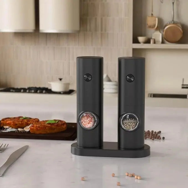 Electric Salt & Pepper Grinder Set displayed on a kitchen countertop with delicious food in the background.