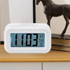 Smart Digital LCD Desk Clock with Temperature Display on a wooden table next to a statue.